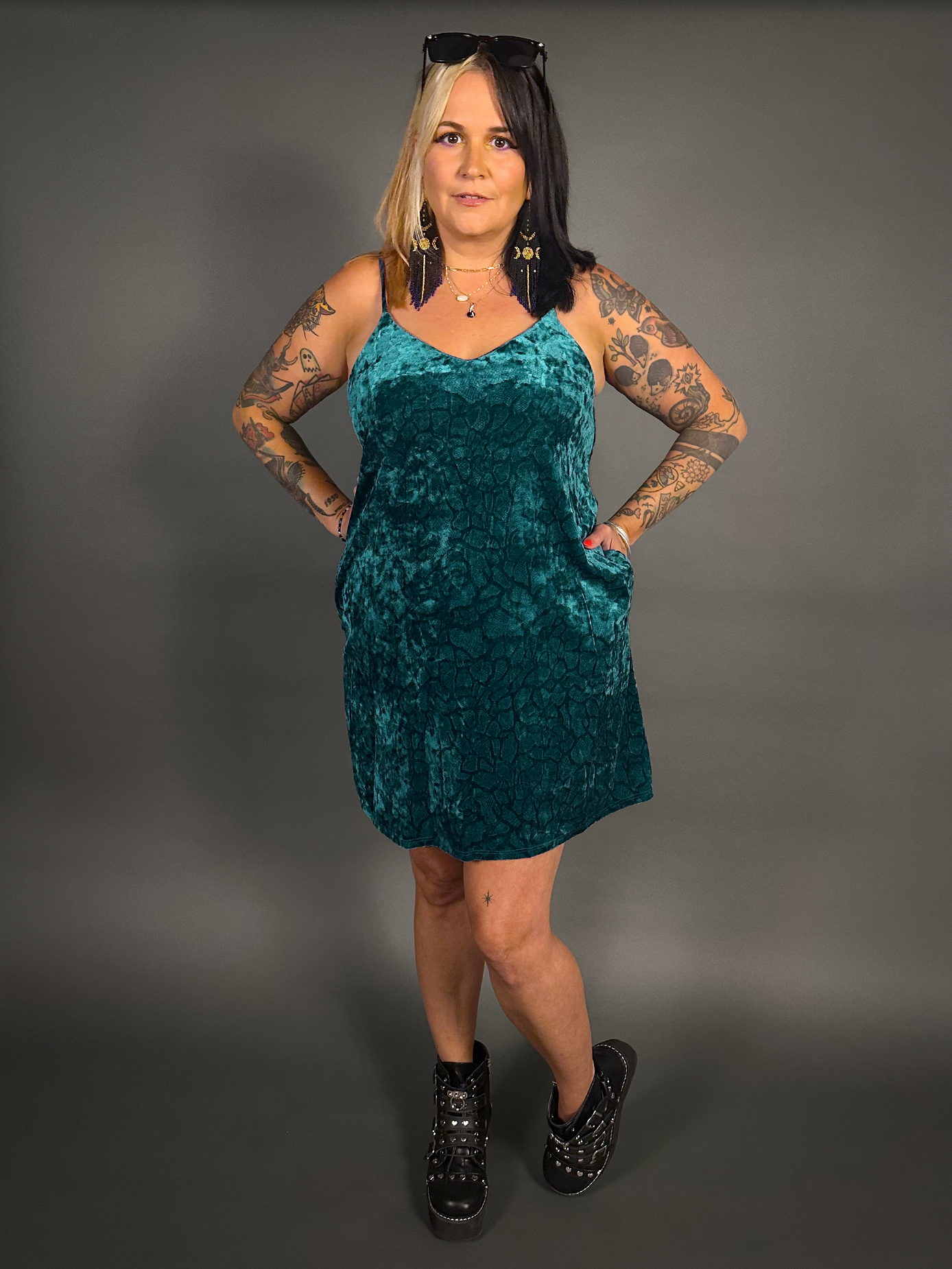Woman wearing a teal velvet dress against a gray background