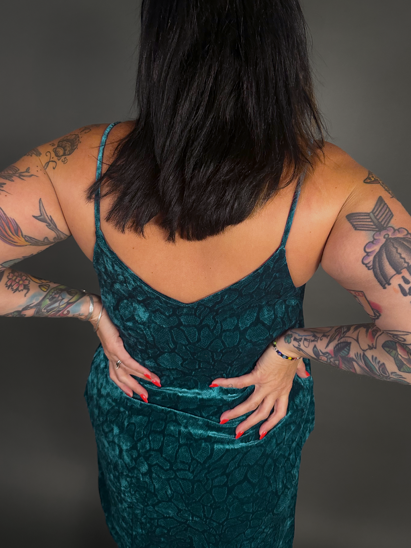 Woman wearing a green velvet dress with tattoos on arms against a dark background