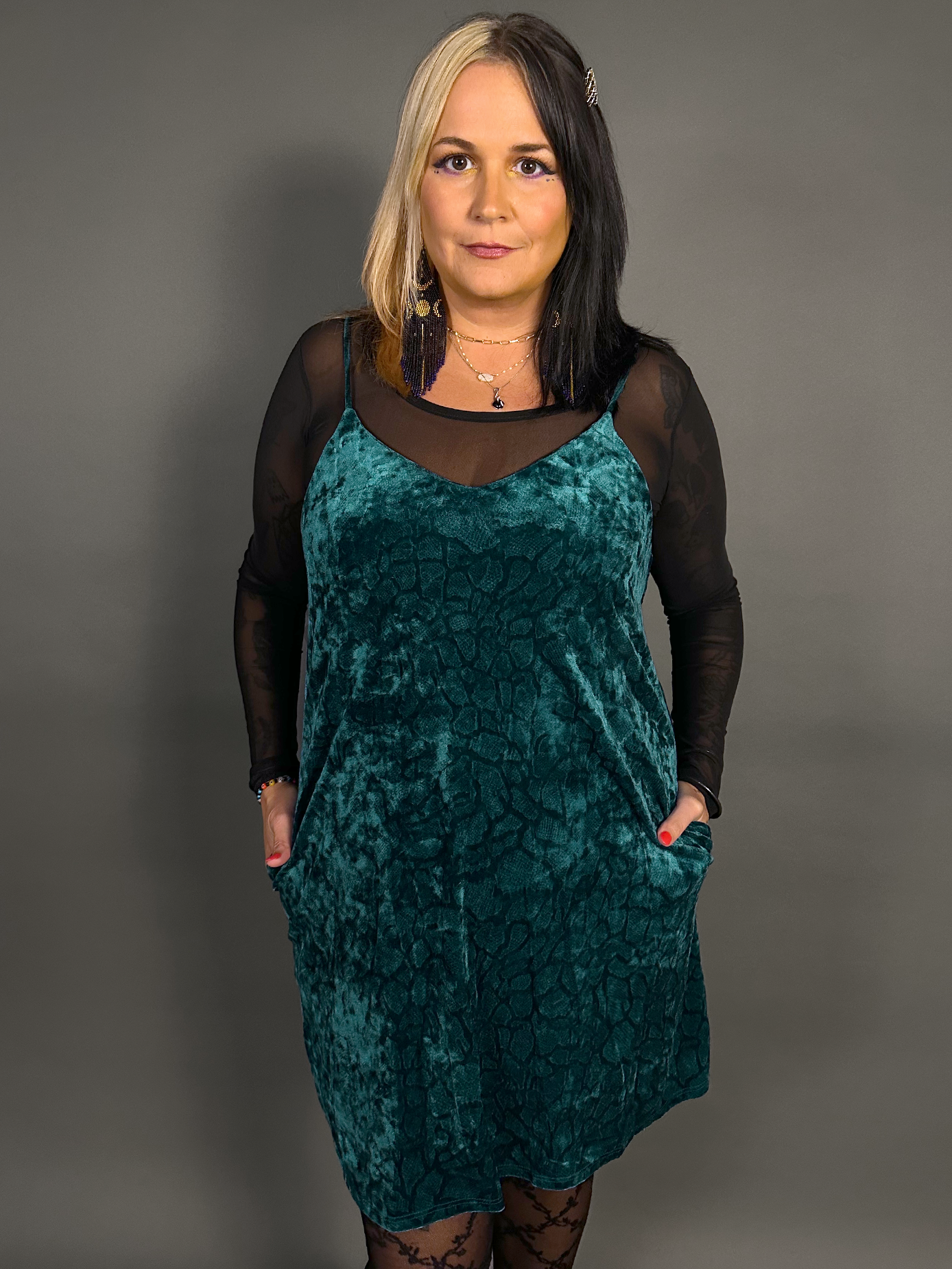 Woman wearing a teal velvet dress with sheer sleeves against a gray background