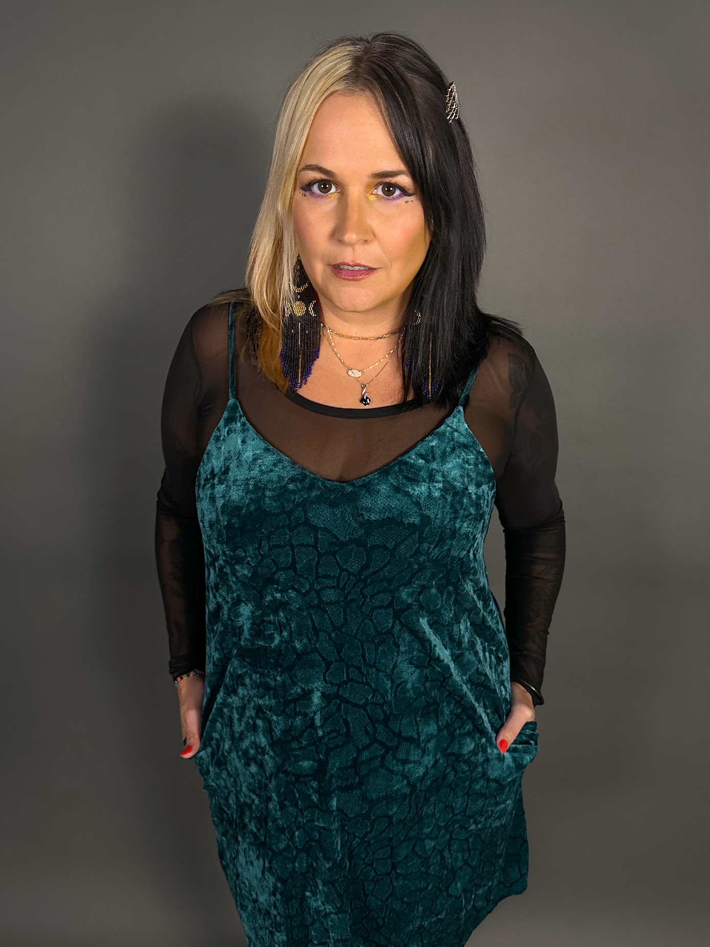 Woman wearing a teal velvet dress with sheer black sleeves against a gray background
