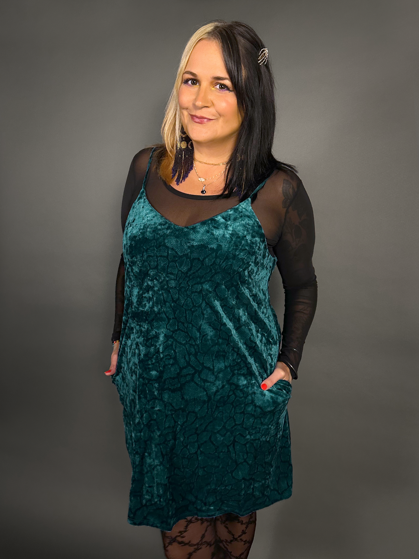 Woman wearing a teal velvet dress with sheer sleeves against a gray background