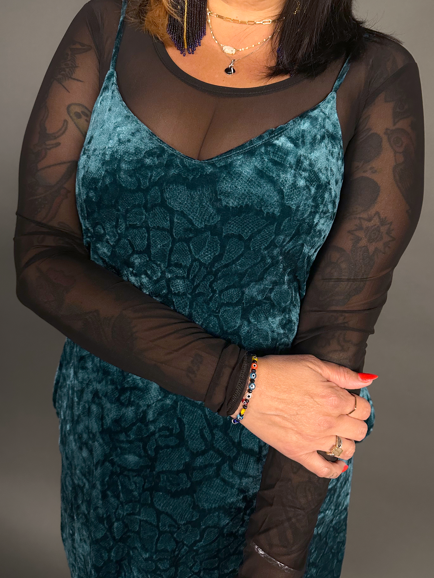 Woman wearing a teal velvet dress with sheer sleeves against a gray background