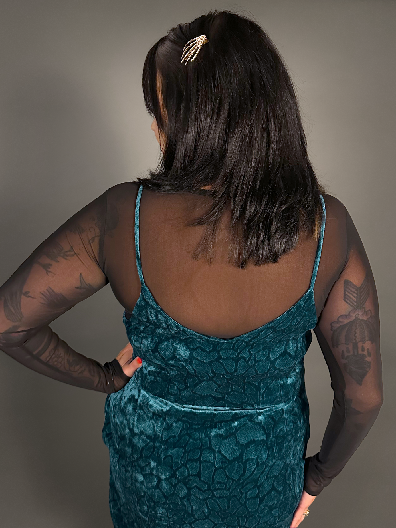 Woman wearing a teal dress with sheer sleeves against a neutral background
