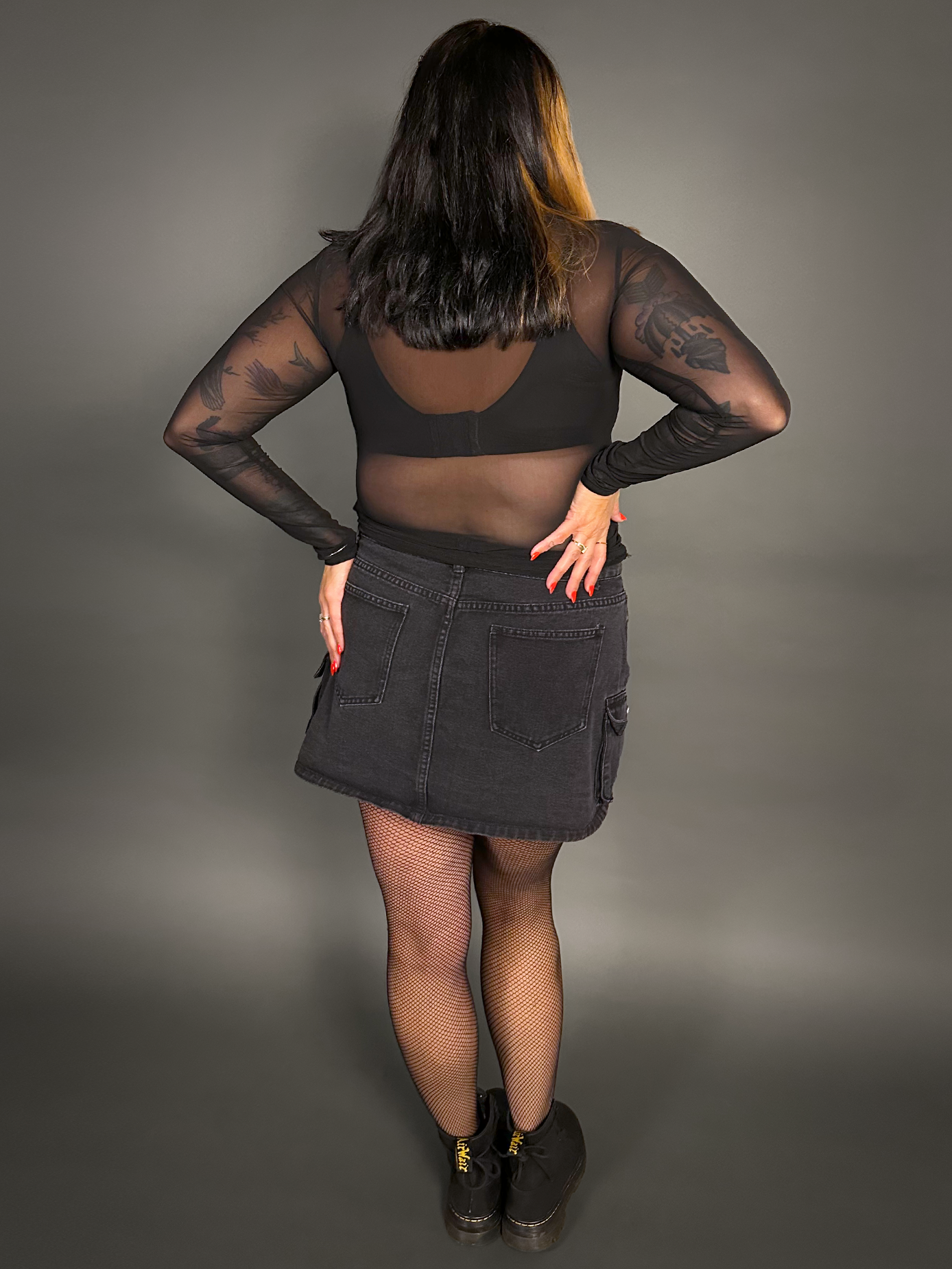Woman wearing a black denim skirt and black top against a gray background