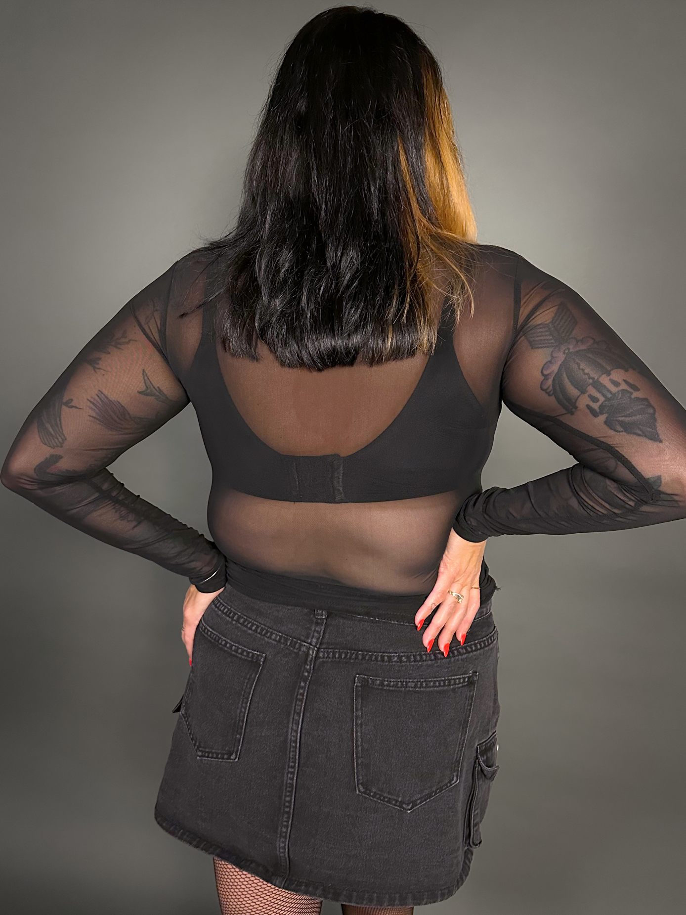 Woman wearing a black outfit with sheer sleeves and a skirt on a gray background