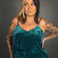 Woman wearing a teal velvet dress with tattoos on arms against a gray background