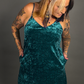Woman wearing a teal velvet dress with tattoos on arms against a gray background