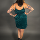 Woman wearing a teal velvet dress with tattoos on arms and legs against a gray background