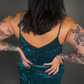 Woman wearing a green velvet dress with tattoos on arms against a dark background