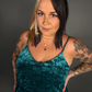 Woman wearing a teal velvet dress with tattoos on arms against a gray background
