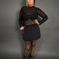 Woman wearing a black floral sheer top and black skirt against a gray background