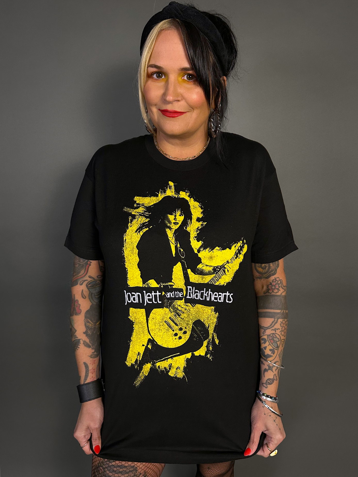 Person wearing a black t-shirt with a graphic design of Joan Jett and the Blackhearts on a gray background