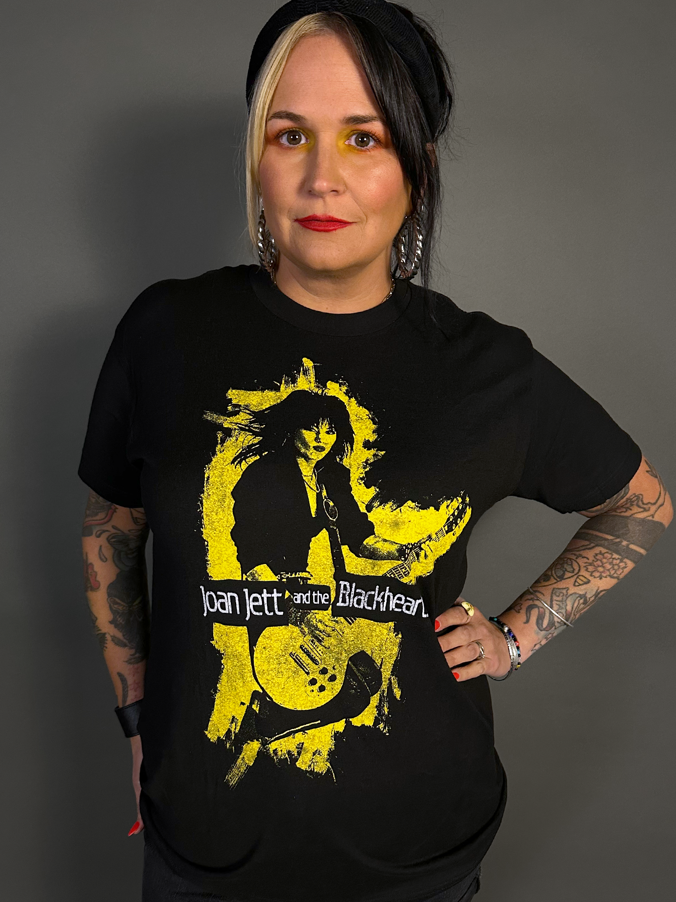 Person wearing a black t-shirt with a graphic design of Joan Jett and the Blackhearts on a gray background