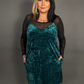 Woman wearing a teal velvet dress with sheer sleeves against a gray background