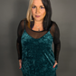 Woman wearing a teal velvet dress with sheer black sleeves against a gray background