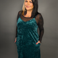 Woman wearing a teal velvet dress with sheer sleeves against a gray background
