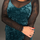 Woman wearing a teal velvet dress with sheer sleeves against a gray background