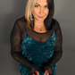 Woman wearing a teal velvet dress with sheer black sleeves against a gray background