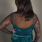 Woman wearing a teal dress with sheer sleeves against a neutral background