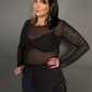 Woman wearing a black outfit with sheer sleeves against a gray background