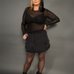 Woman wearing a black outfit with sheer sleeves and a skirt on a gray background