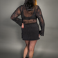 Woman wearing a sheer top and skirt with spider web design on a gray background