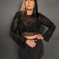 Woman wearing a black sheer top with spiderweb design and skirt against a gray background