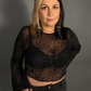 Woman wearing a black sheer top with spiderweb design and skirt against a gray background